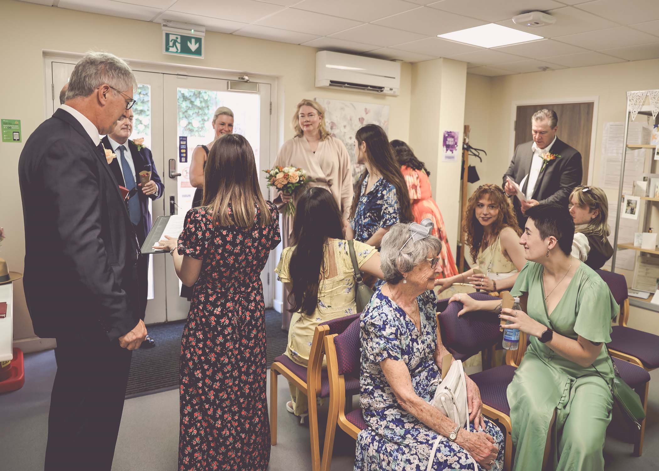 A bridal party mingling in Woodbridge Registry Office waiting room on a wedding day in Woodbridge captured by Suffolk Wedding Photographer Hayley Denston Photography